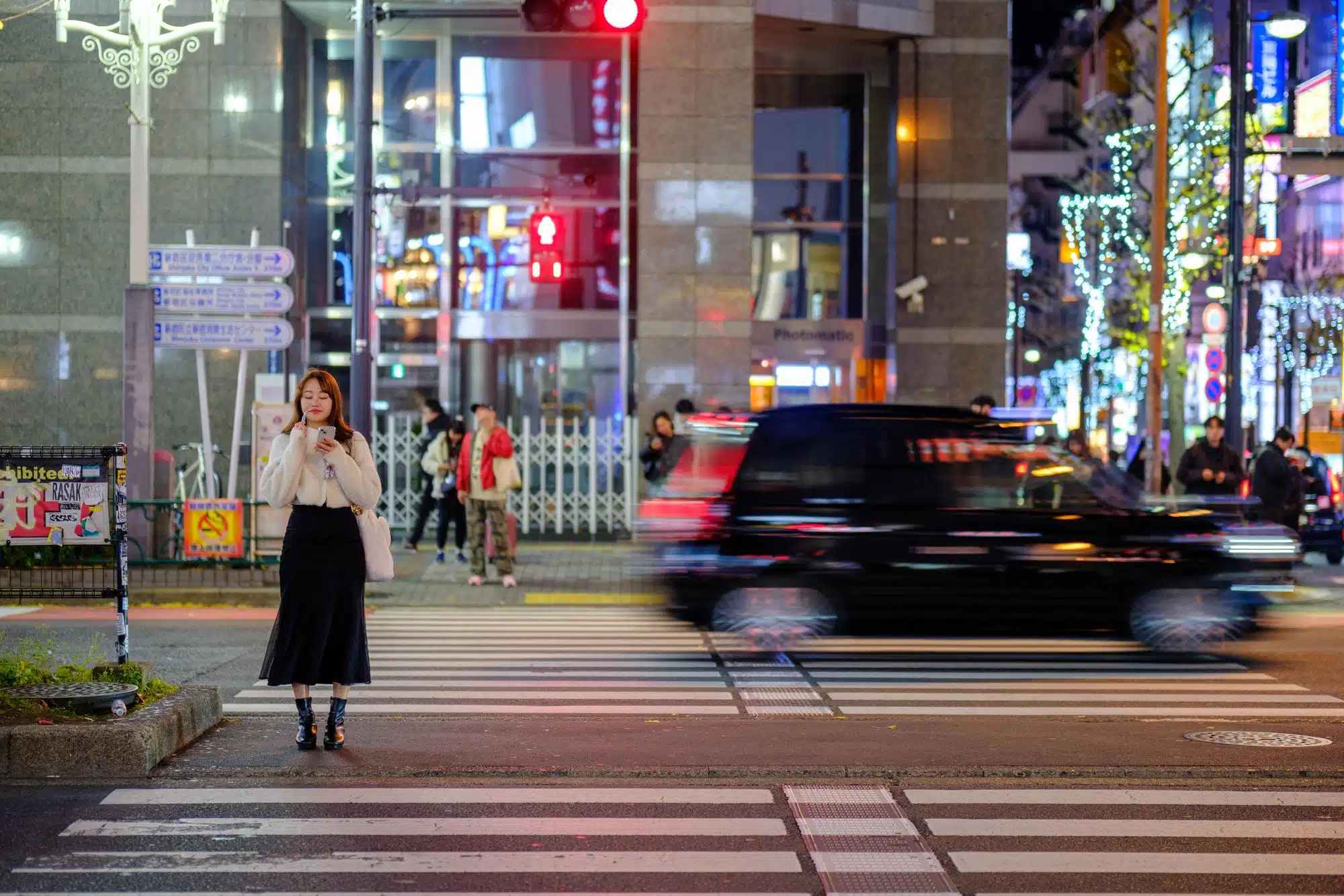 A lady adjusts her make-up while looking at her phone in the middle of a street in Shinjuku, Tokyo.