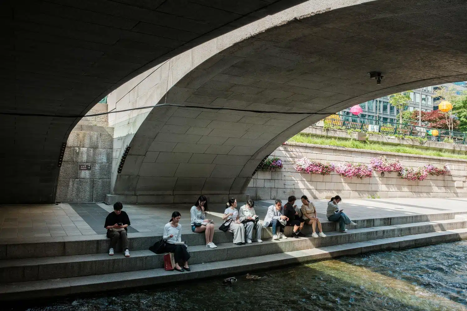 cheonggyecheon-seoul-summer-2026-bridge People relax under a bridge along the Cheonggyecheon Stream in Seoul.