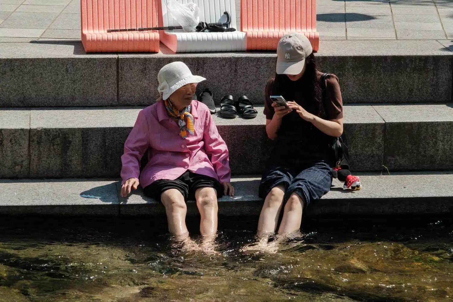 cheonggyecheon-women-20260523 An elderly woman and a young one soak their feet in Cheonggyecheon stream in Seoul.