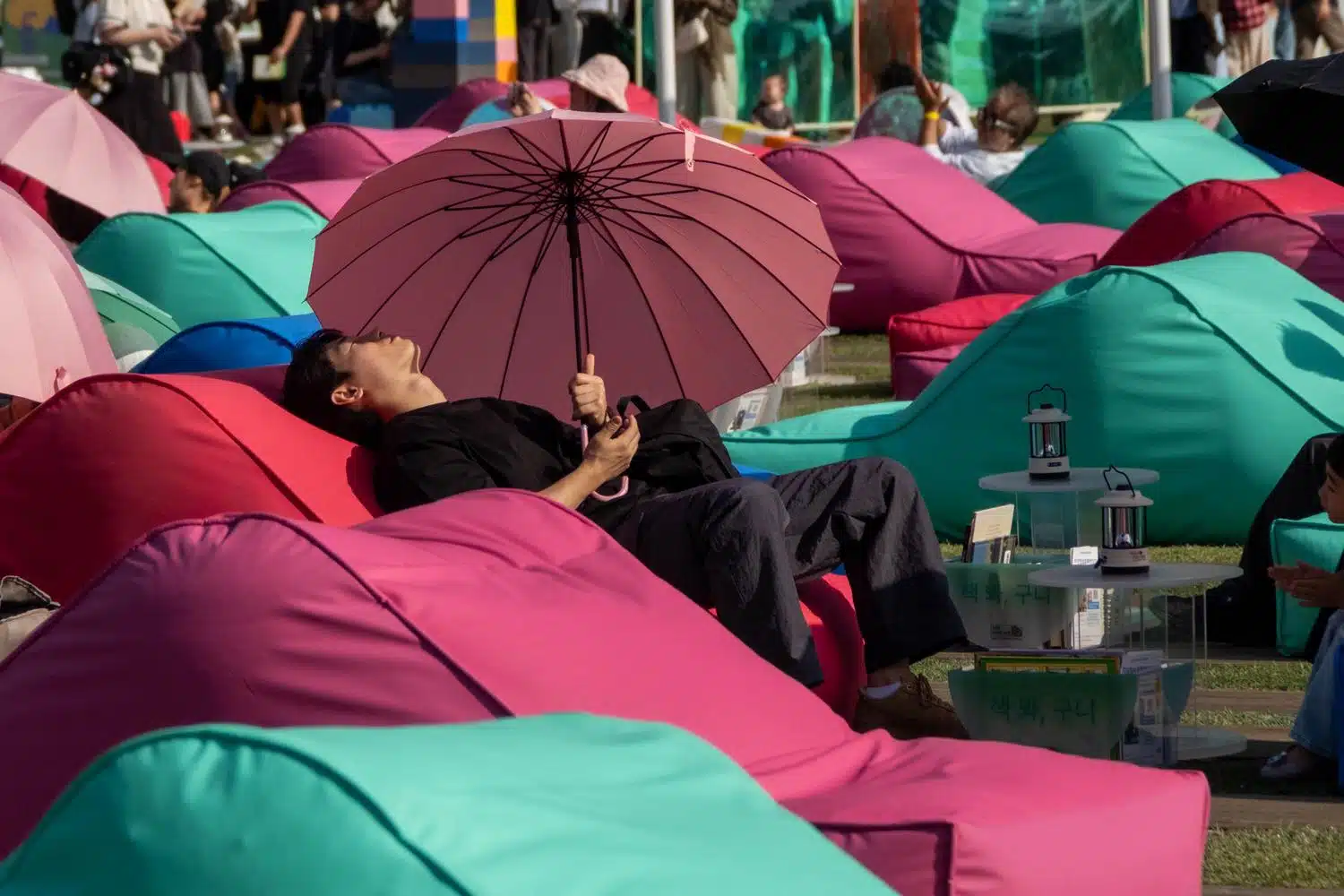 seoul-outdoor-library-summer-2026-1 A man rests under an umbrella in a public sofa during the Seoul Outdoor Library event in May 2026.