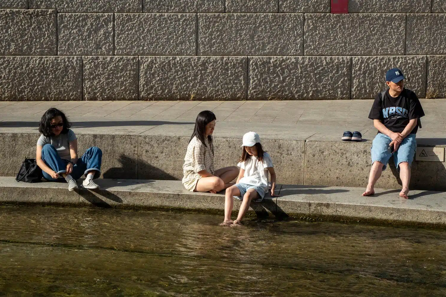 seoul-outdoor-library-summer-2026-10 A family relaxes along Cheonggyecheon stream in central Seoul during the weekend