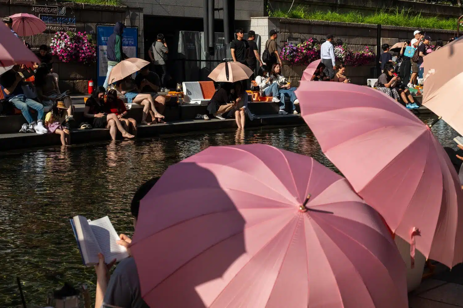 seoul-outdoor-library-summer-2026-11 People relax along the Cheonggyecheon Stream in Seoul