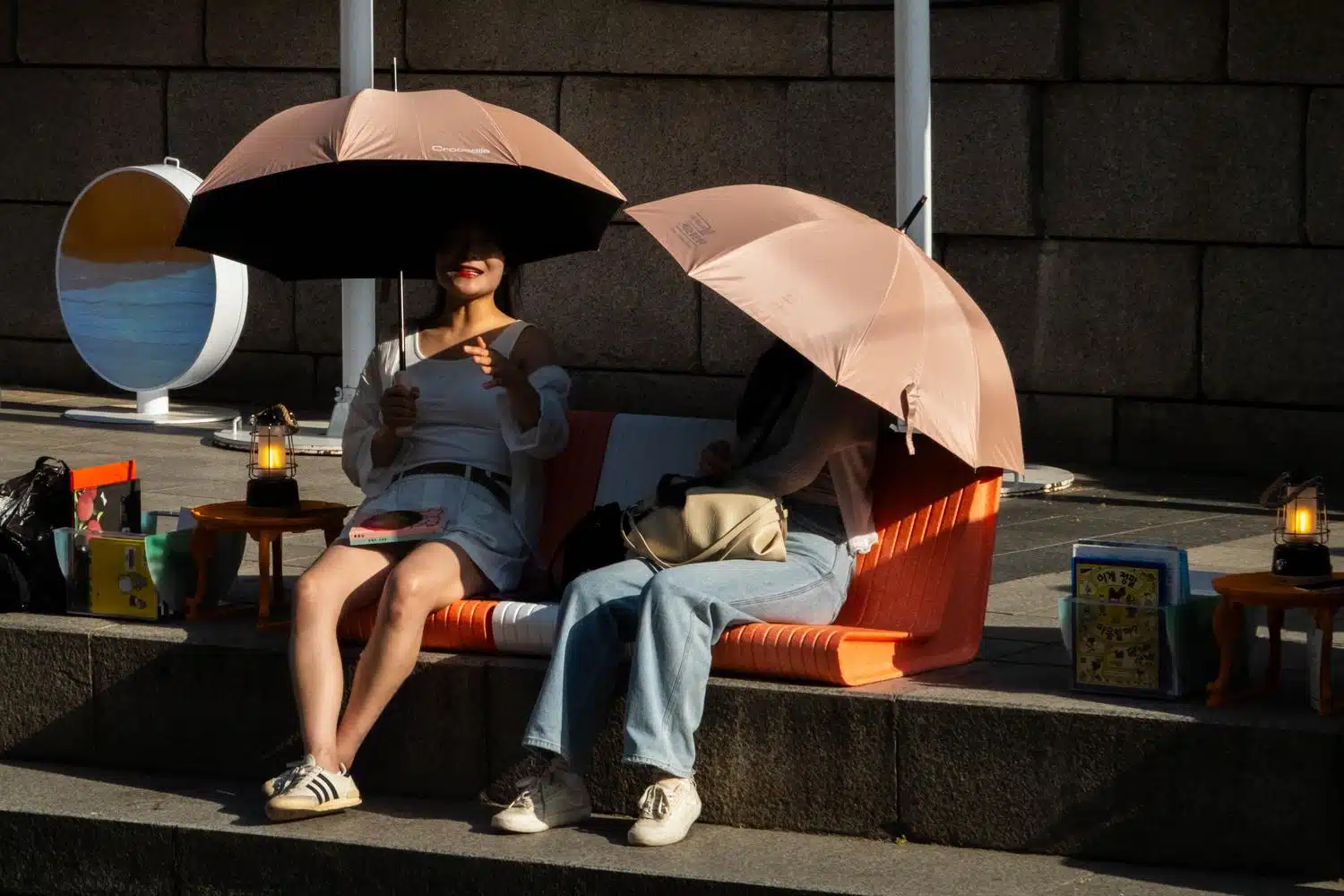seoul-outdoor-library-summer-2026-21 Two women relax under umbrellas along Cheonggyecheon stream in central Seoul