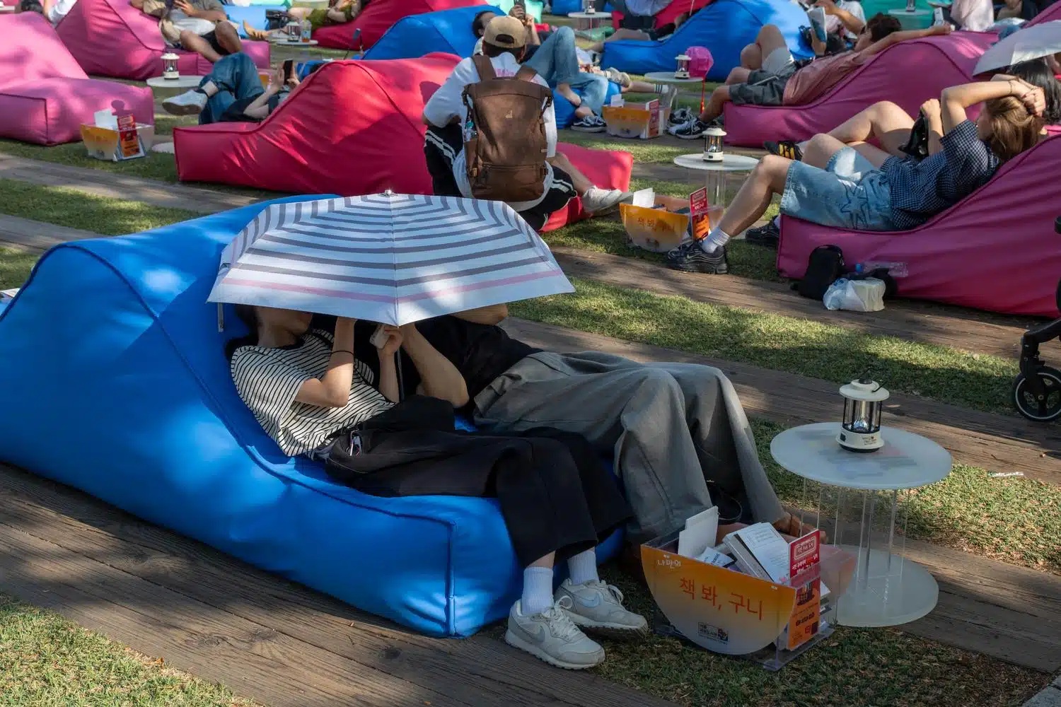 seoul-outdoor-library-summer-2026-9 A couple rests on a public sofa under an umbrella at Seoul Plaza's Outdoor Library