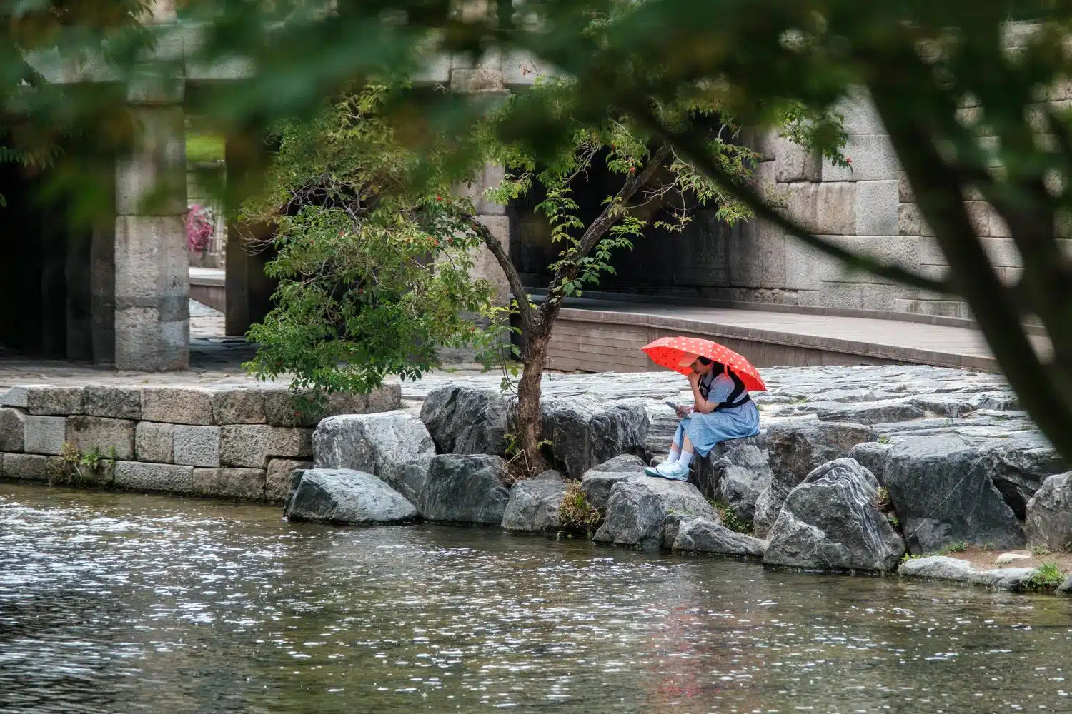 cheonggyecheon-seoul-red-umbrella A woman relaxes under a red umbrella along Cheonggyecheon stream in Seoul.