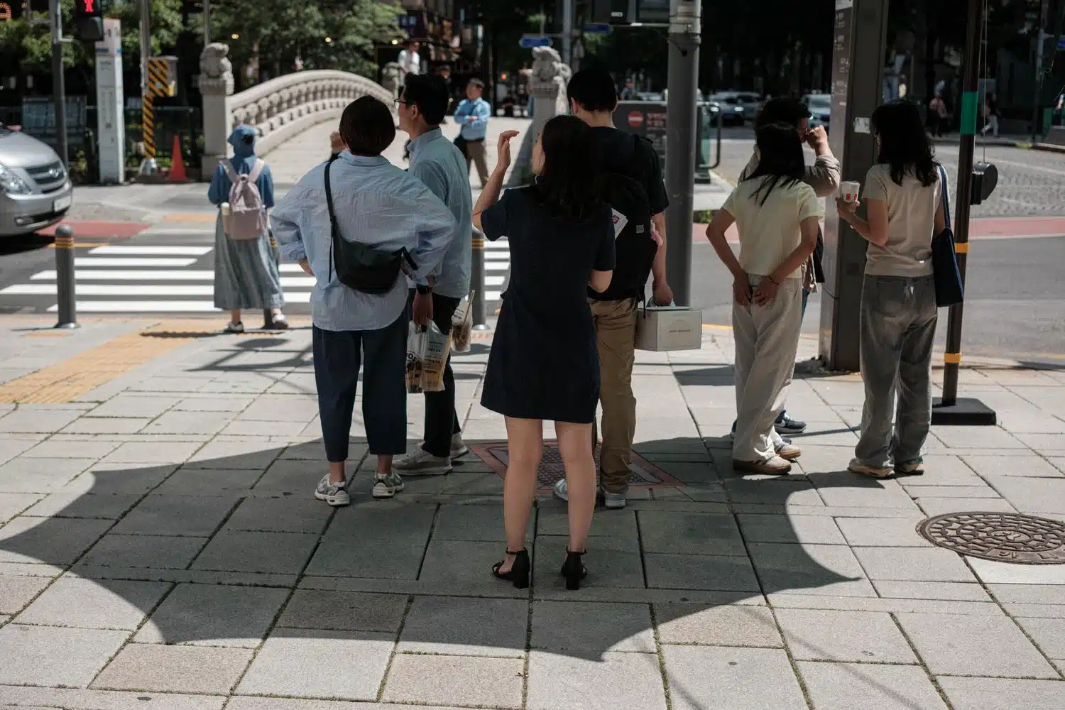 seoul-street-umbrella-crossing-summer-2026 People wait to cross a street under a giant umbrella in Seoul.
